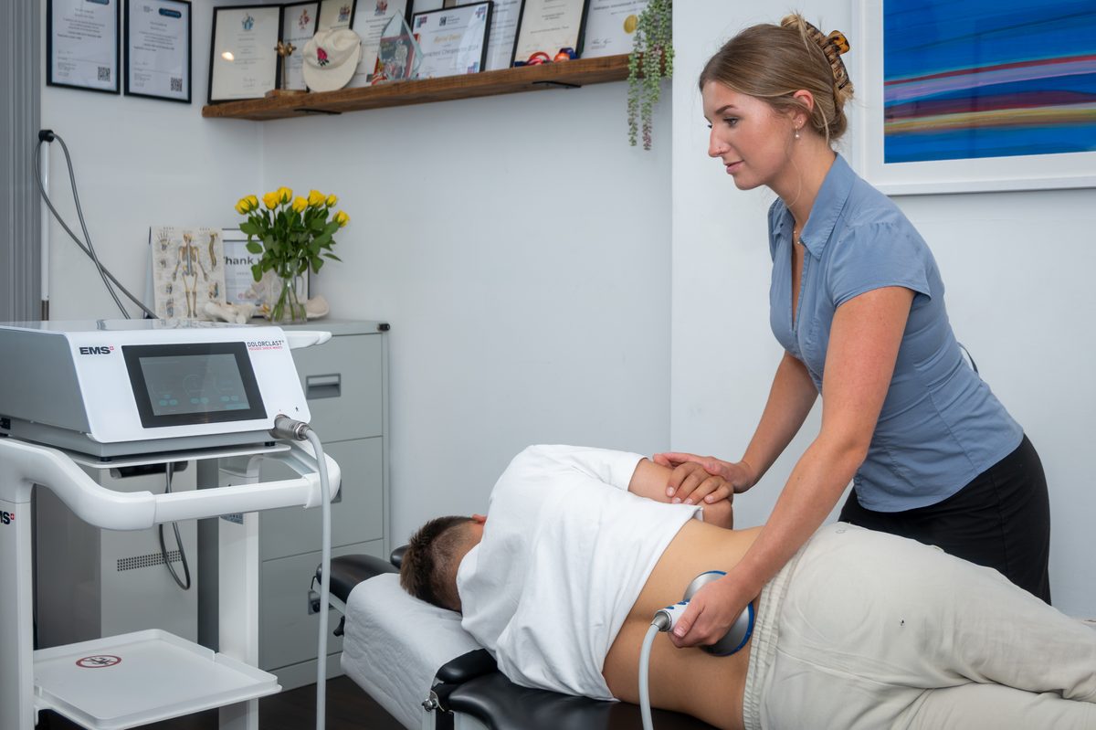 Anya using the shockwave machine on a patient’s lower back